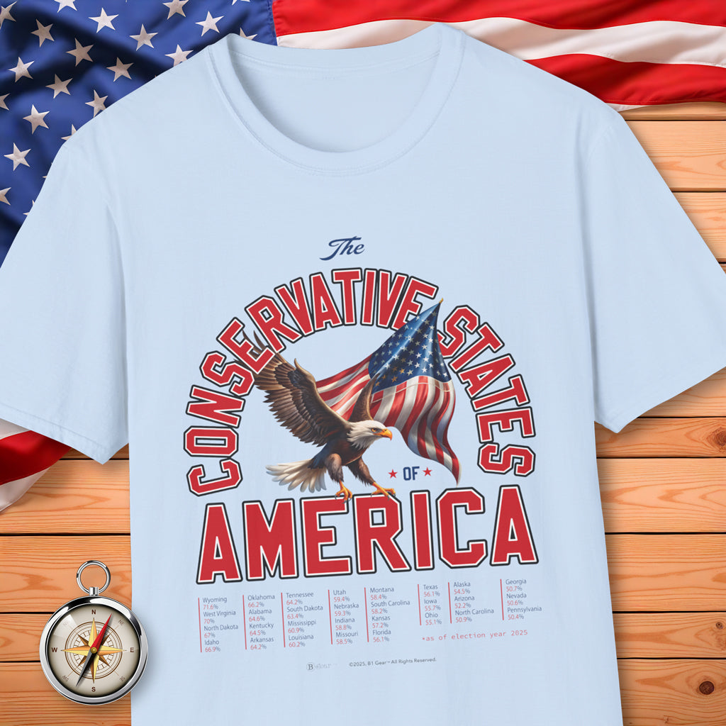 Light blue t-shirt with 'The Conservative States of America' graphic on a wooden surface with an American flag in the background.